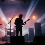 Silhouettes of a rock band performing on a smoky, light-filled concert stage