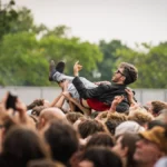A fan crowd-surfs at an IDLES festival show, capturing IDLES live in 2026