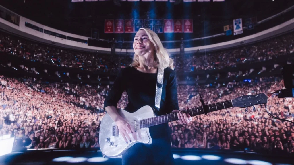 Phoebe Bridgers with a silver guitar in front of a full arena on The Lost Tour